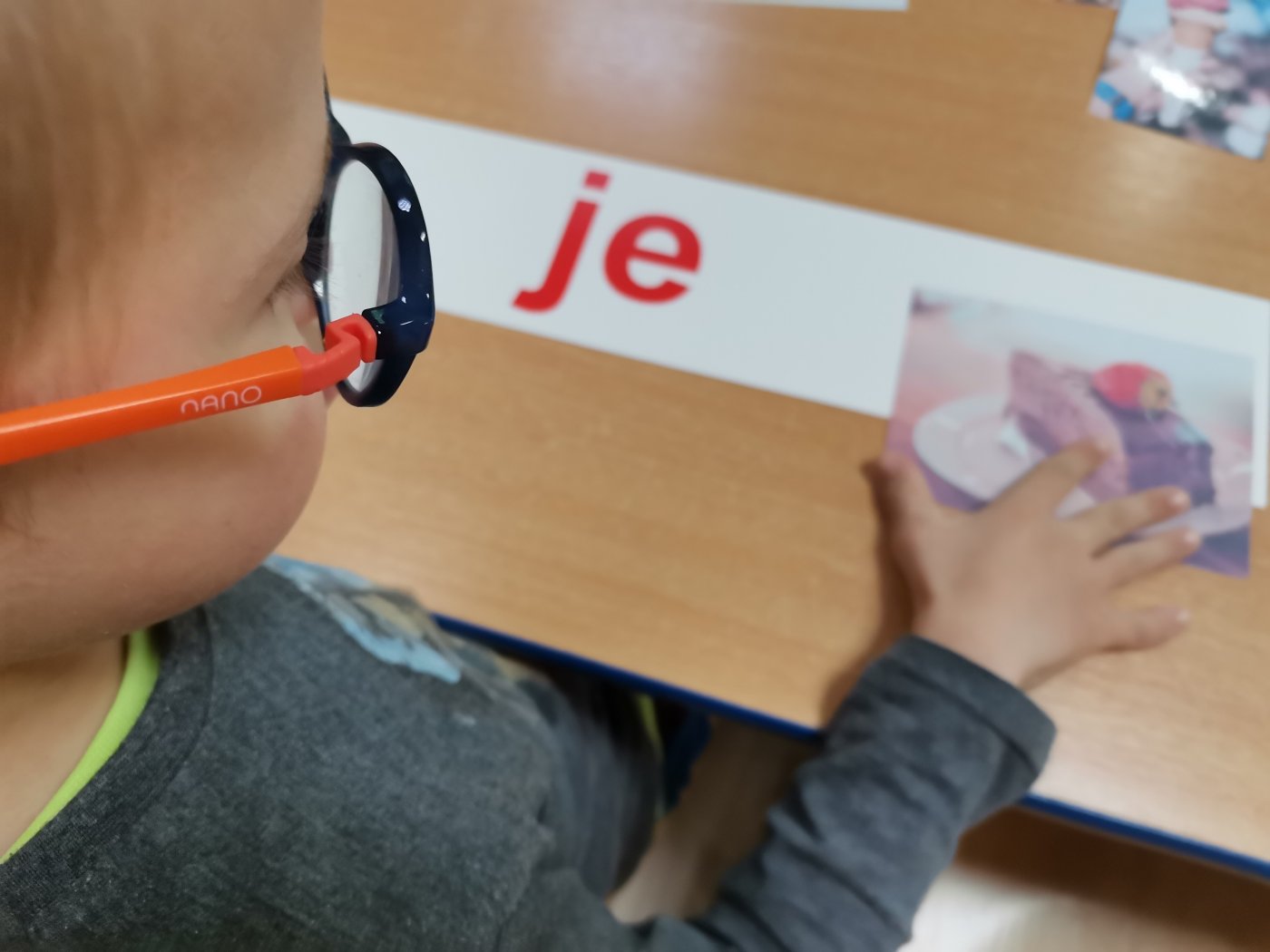 Na zdjęciu widać chłopca w okularach z czerwonymi oprawkami, który uczy się siedząc na krześle przy stole.