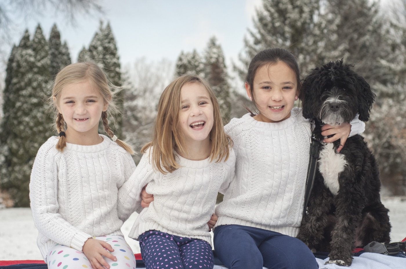Trzy dziewczynki z psem na tle zimowego krajobrazu.