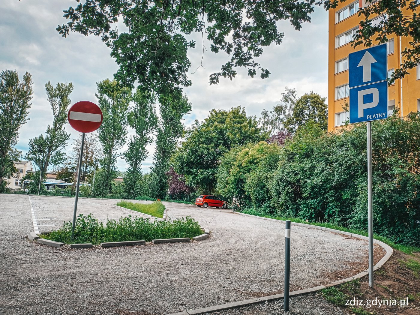 parking z nową nawierzchnią, widoczne oznakowanie pionowe, budynek i zieleń