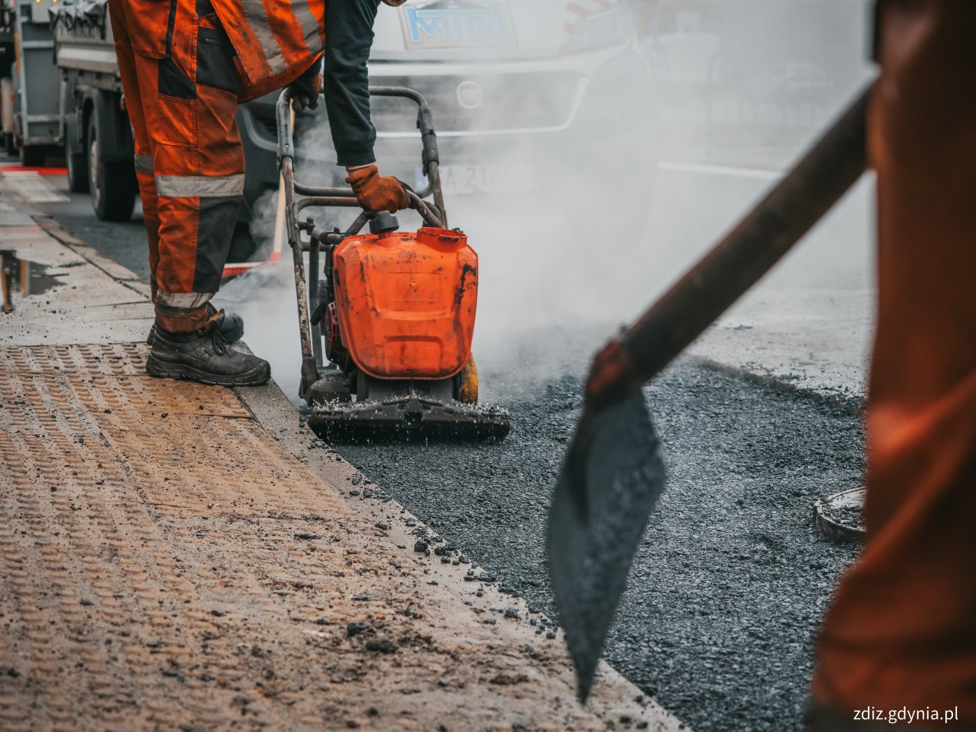 trwające roboty drogowe, widoczny remont nawierzchni. Pracujące urządzenia, na pierwszym planie łopata.