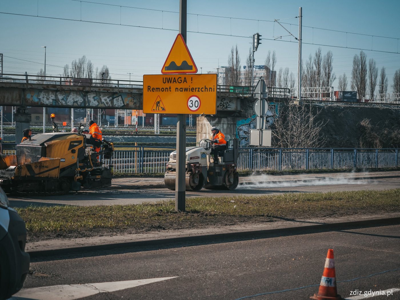 trwające naprawy nawierzchni, widoczne oznakowanie, pojazd naprawiający nawierzchnię