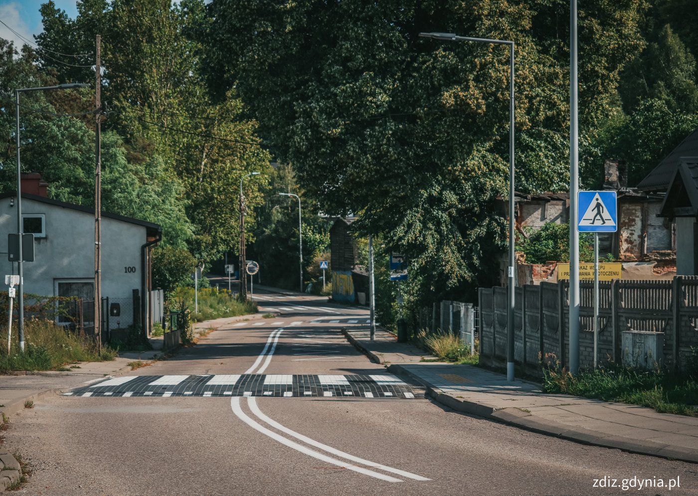 widok na jezdnię i wyniesione przejście dla pieszych. Widoczne oznakowanie oraz chodnik i zieleń