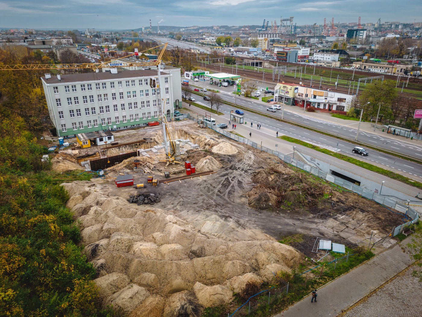 Plac budowy hali sportowej przy ulicy Morskiej w Zespole Szkół Hotelarsko-Gastronomicznych z lotu ptaka, widać wykopy budowlane, budynek szkoły, na dalszym planie ulica morska i port