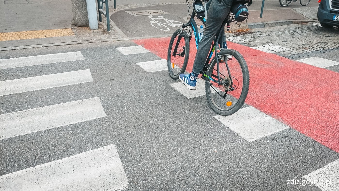 rower przejeżdżający przez ulicę przejazdem rowerowym widoczna ulica z oznakowaniem poziomym, rowerzysta i rower