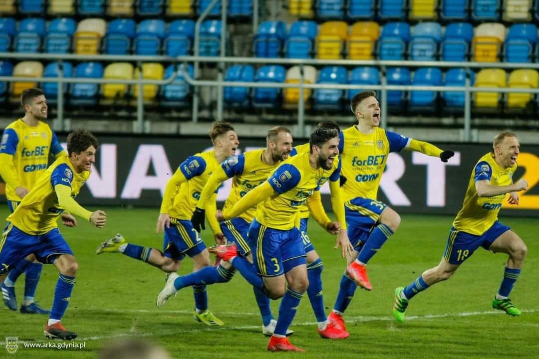 Zawodnicy Arki Gdynia cieszący się na boisku z wygranej, w klubowych żółto-niebieskich strojach.