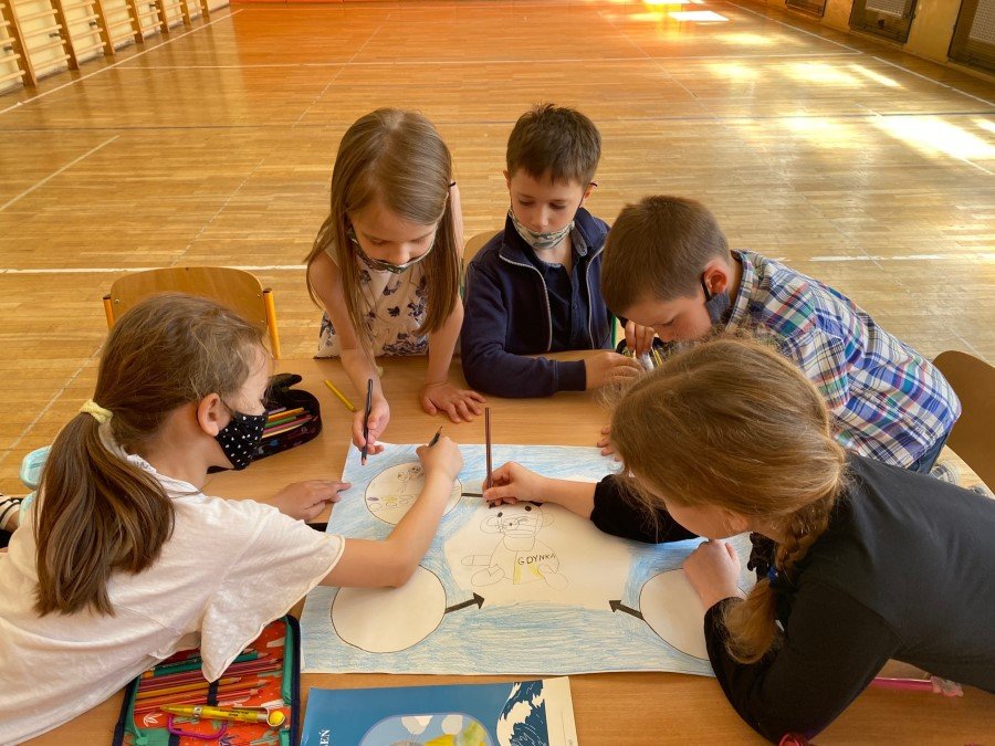 Piątka dzieci (trzy dziewczyny i dwójka chłopców) podczas rysowania. Znajdują się na szkolnej sali.