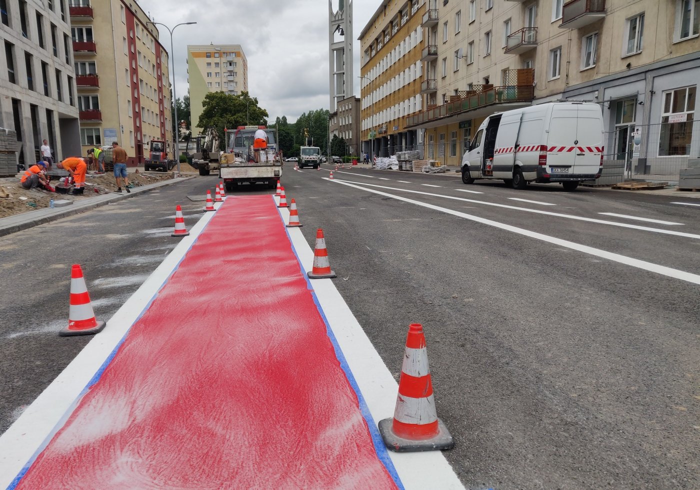 Fragment ulicy Armii Krajowej w Gdyni z namalowaną na asfalcie drogą dla rowerów. W tle robotnicy i budynki