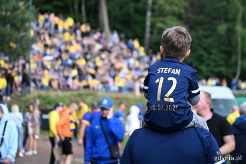 Górka przy ulicy Ejsmonda, grupa kibiców na skarpie, na pierwszym planie dziecko w koszulce z numerem 12, siedzi na ramionach mężczyzny, widoczne żółto-niebieskie barwy