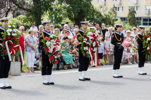 Marynarze trzymają biało czerwone wieńce, w tle mieszkańcy
