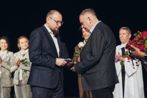 Dwaj mężczyźni w garniturach na scenie, w tle aktorzy