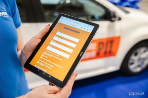 Kobieta trzyma w rękach tablet z widocznym na nim formularzem zgłoszeń 