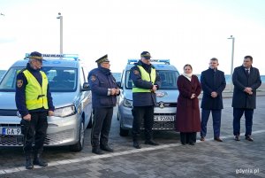Od lewej: Łukasz Kobus &ndash; sekretarz miasta i dyrektor generalny Urzędu Miasta Gdyni, Robert Ronduda &ndash; naczelnik Wydziału Zarządzania Kryzysowego i Ochrony Ludności, prezydent Gdyni Aleksandra Kosiorek oraz Andrzej Bień &ndash; komendant Straży Miejskiej w Gdyni (w środku) i strażnicy miejscy podczas oficjalnego przekazania nowych radiowoz&oacute;w