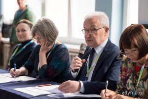 Jury siedzące przy biurku, mężczyzna mówi prze mikrofon
