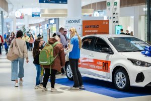 Dorośli i dzieci przy aucie, obok hostesa w niebieskiej koszulce