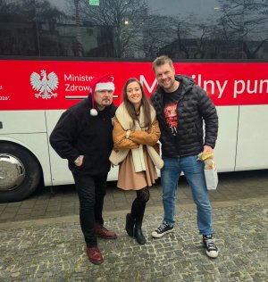 Dwójka młodych ludzi i mężczyzna w czapce świętego Mikołaja na tle ambulansu 