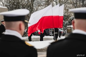 Biało-czerwone flagi powiewające przy pomniku Polski Morskiej z okazji 78. rocznicy zakończenia walk o Gdynię. Na pierwszym planie dwaj stojący w rzędzie marynarze // fot. Kamil Złoch