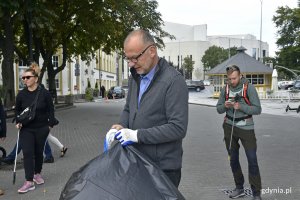 Wiceprezydent Gdyni Michał Guć nakłada biało-niebieskie rękawiczki. W jednej z rąk trzyma czarny worek na śmieci // fot. Magdalena Czernek