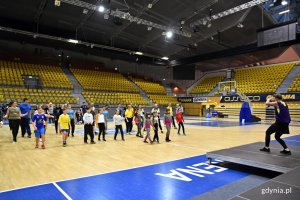 Grupa dzieci oraz instruktor podczas ćwiczeń na hali Gdynia Arena. 