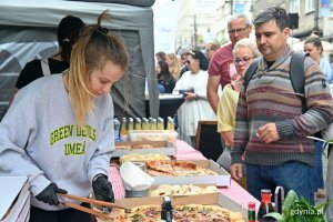 Stoisko z pizzą na festiwalu „Kulinarna Świętojańska”. Na pierwszym planie: młoda kobieta łapie kawałek pizzy. Obok stoiska kolejka uczestników, którzy chcą spróbować wyrobów // fot. Magdalena Czernek