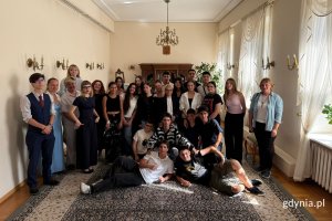 Zdjęcie grupowe zrobione podczas spotkania w sali wizytowej. Ludzie w młodym wieku oraz ich opiekunowe i przedstawiciele Młodzieżowej Rady Miasta stojący w kilku rzędach. Na pierwszym planie dwoje mężczyzn w pozycji leżącej, a za nimi czwórka mężczyzn trzymająca się za ramiona. 