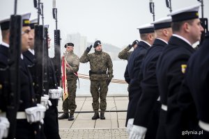 Maszerują marynarze z karabinami, mijając stojących żołnierzy ze sztandarami.