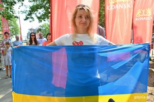 Ukrainka uczestnicząca w uroczystości otwarcia skweru Bohaterskiego Mariupola - trzyma w rękach ukraińską flagę. Stoi na tle czerwonych flyerów z logo Gdańska // fot. Magdalena Czernek