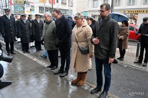 Grupa osób składa hołd pod pomnikiem.