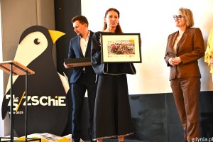 Dwie kobiety na sceniem, jedna trzyma fotografię