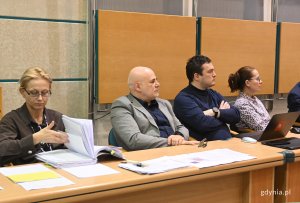 na zdjęciu ludzie przy biurku i kobieta przeglądająca dokumentację