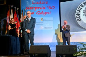 Andrzej Kołodziej, prezes Fundacji Pomorska Inicjatywa Historyczna, przemawia podczas uroczystości w sali koncertowej Zarządu Morskiego Portu Gdynia. Z tyłu - prezydent Gdyni Wojciech Szczurek bije brawo // fot. Magdalena Czernek