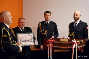 Strażacy wręczają strażakowi upominki - grafikę i szble.