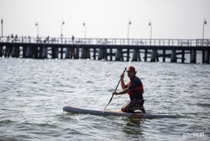 Plaża w Orłowie. Mężczyzna płynie na desce odpychając się wiosłem, w tle molo. Fot, Przemysław Kozłowski