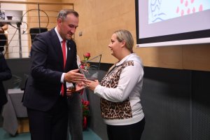 Kobieta odbiera nagrodę z rąk mężczyzny w garniturze