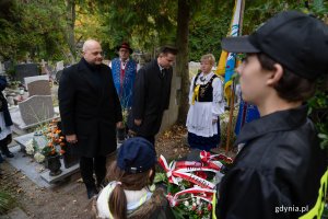Mężczyzna w czarnym garniturze i kobieta w regionalnym stroju nad grobem.