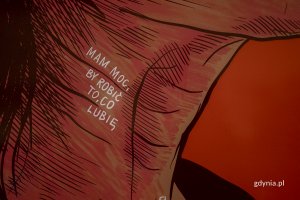 Ilustracja w kolorze czerwonym. Przedstawia ludzkie gardło, na którym znajduje się biały napis "Mam moc, żeby robić to co lubię".