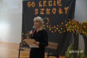 Stojąca kobieta mówiąca do mikrofonu w szkolnej hali sportowej