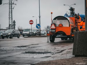 roboty drogowe, pracownicy zabezpieczają ubytek w jezdni, w tle samochód