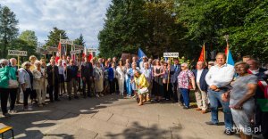 Grupa ludzi z tabliczkami pod pomnikiem
