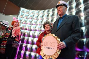 Seniorzy pozują do zdjęcia z napisem 100 Gdynia