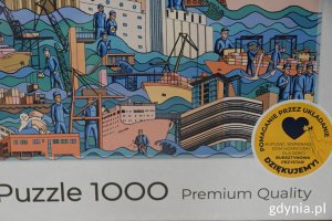 Fragment pudełka z puzzlami i napisem: puzzle 1000, pomaganie poprzez układanie, kupując wspierasz Dom Hospicyjny dla Dzieci „Bursztynowa Przystań”, dziękujemy