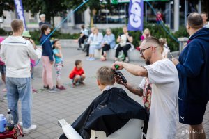 Mężczyzna strzyże chłopca siedzącego na fotelu fryzjerskim ustawionym na chodniku.