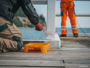 malowanie drewnianych elementów mola, widoczni pracownicy wykonujący prace w odzieży ochronnej