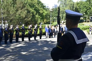 Marynarz stojący z bronią w ręku pełni wartę honorową pod pomnikiem podczas uroczystości na Cmentarzu Wojennym w Redłowie. W tle salutujący przedtawiciele Marynarki Wojennej