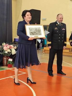 Pionowe zdjęcie - na pierwszym planie dyrektor z obrazem przedstawiającym łódź, w tle mężczyzna w wojskowym mundurze.