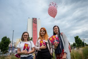 Trzy uczestniczki festiwalu "Miasto Słowa" na tle hotelu Mercure i wiszącego na nim czerwono-czarnego baneru Nagrody Literackiej GDYNIA. W rękach trzymają książki Aleksandry Radomskiej p. Kobieta po prawej na w drugiej ręce dwa kolorowe balony // fot. Anna Rezulak 