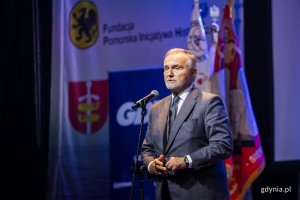 Prezydent Gdyni Wojciech Szczurek przemawiający w sali koncertowej Zarządu Morskiego Portu Gdynia podczas uroczystości z okazji 43. rocznicy strajków sierpniowych i podpisania porozumień sierpniowych. W tle sztandary oraz logo Fundacji Pomorska Inicjatywa Historyczna i miasta Gdyni // fot. Karol Stańczak