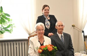 Para senior&oacute;w na krzesłach za nimi stoi kobieta w ciemnej marynarce