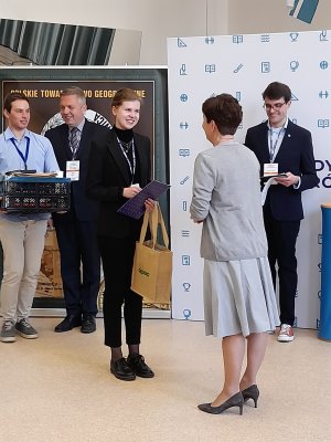 Nagrodę dla najlepszej laureatki wręczyła Ewa Śliwińska, stojąca tyłem do obiektywu, dyrektor gdyńskiego VI LO. W tle dwóch uczniów z nagrodami, ścianka III LO i Polskiego Towarzystwa Geograficznego.