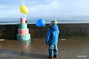 Jeden z najmłodszych uczestników karnawałowej zabawy na bulwarze Nadmorskim przy jednym z kolorowych tortów. Chłopczyk trzyma w ręku kolorowe balony // fot. Magdalena Czernek