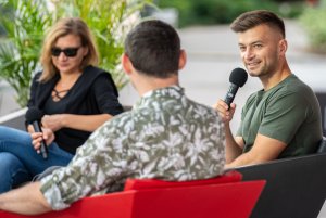 Po lewej Barbara Klicka w ciemnej marynarce oraz czarnych okularach, na środku Jakub Małecki - autor książki "Saturnin" - w zielonym t-shircie oraz po prawej Maciej Jakubowiak we wzorzystej koszuli siedzą w Muszli na placu Grunwaldzkim w Gdyni podczas spotkania w ramach festiwalu "Miasto Słowa" // fot. Anna Rezulak